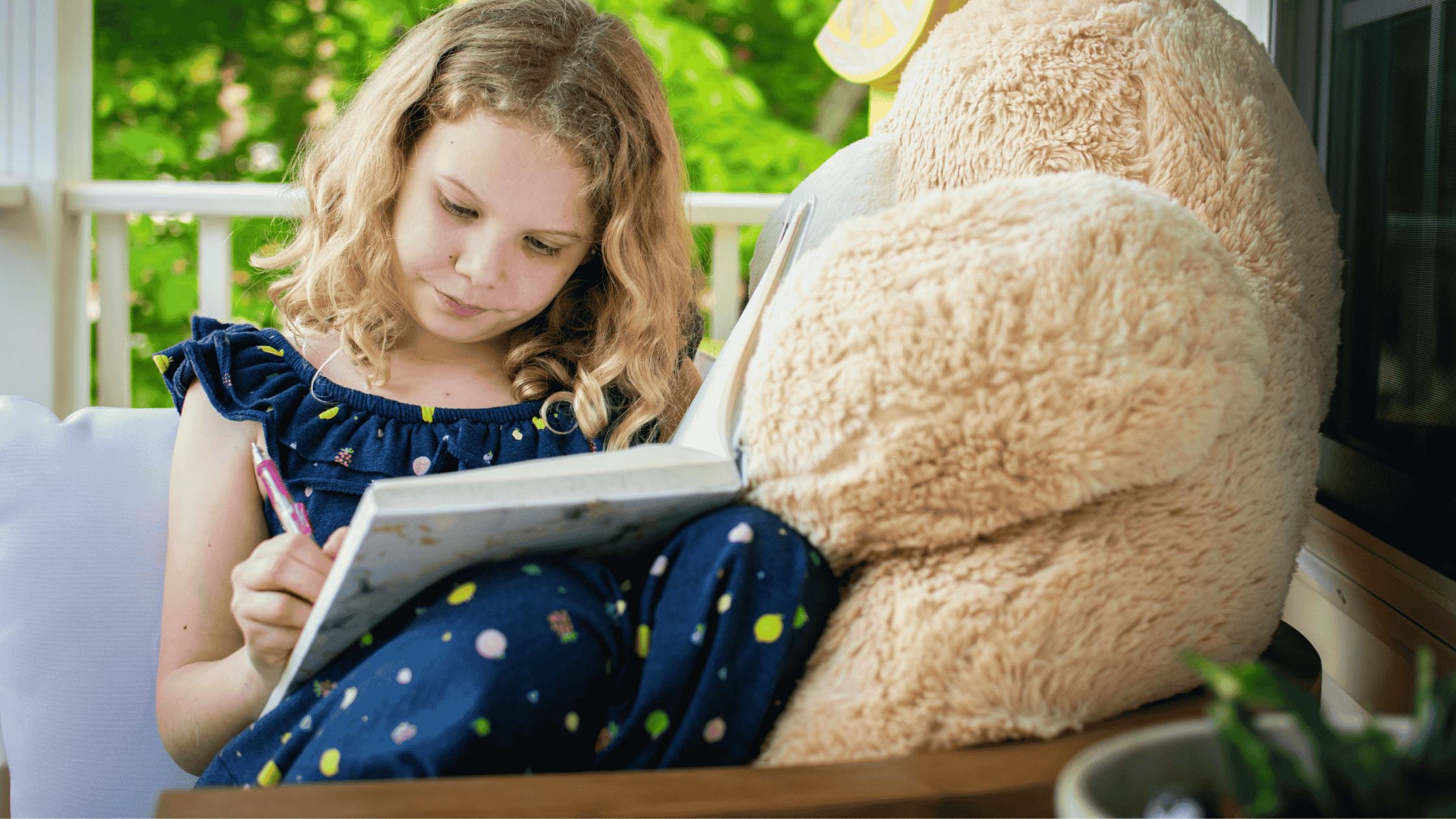 A young girl with curly hair writing in a journal on a sunny porch, seated next to a large teddy bear capturing the comfort and creativity of journal prompts for kids