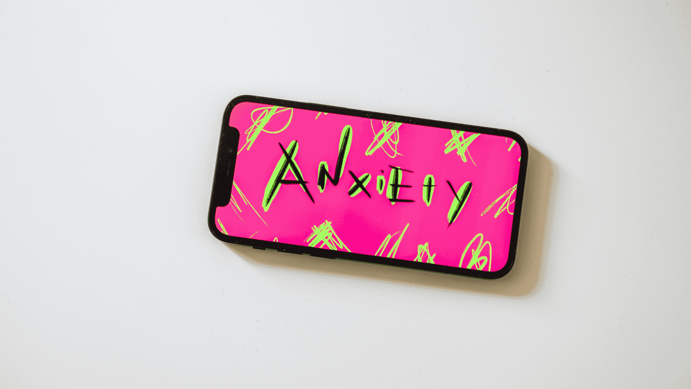 A smartphone lying flat with a bold pink screen displaying the word 'Anxiety' in graphic lettering&mdash;representing how journaling prompts for mental health can help manage anxiety