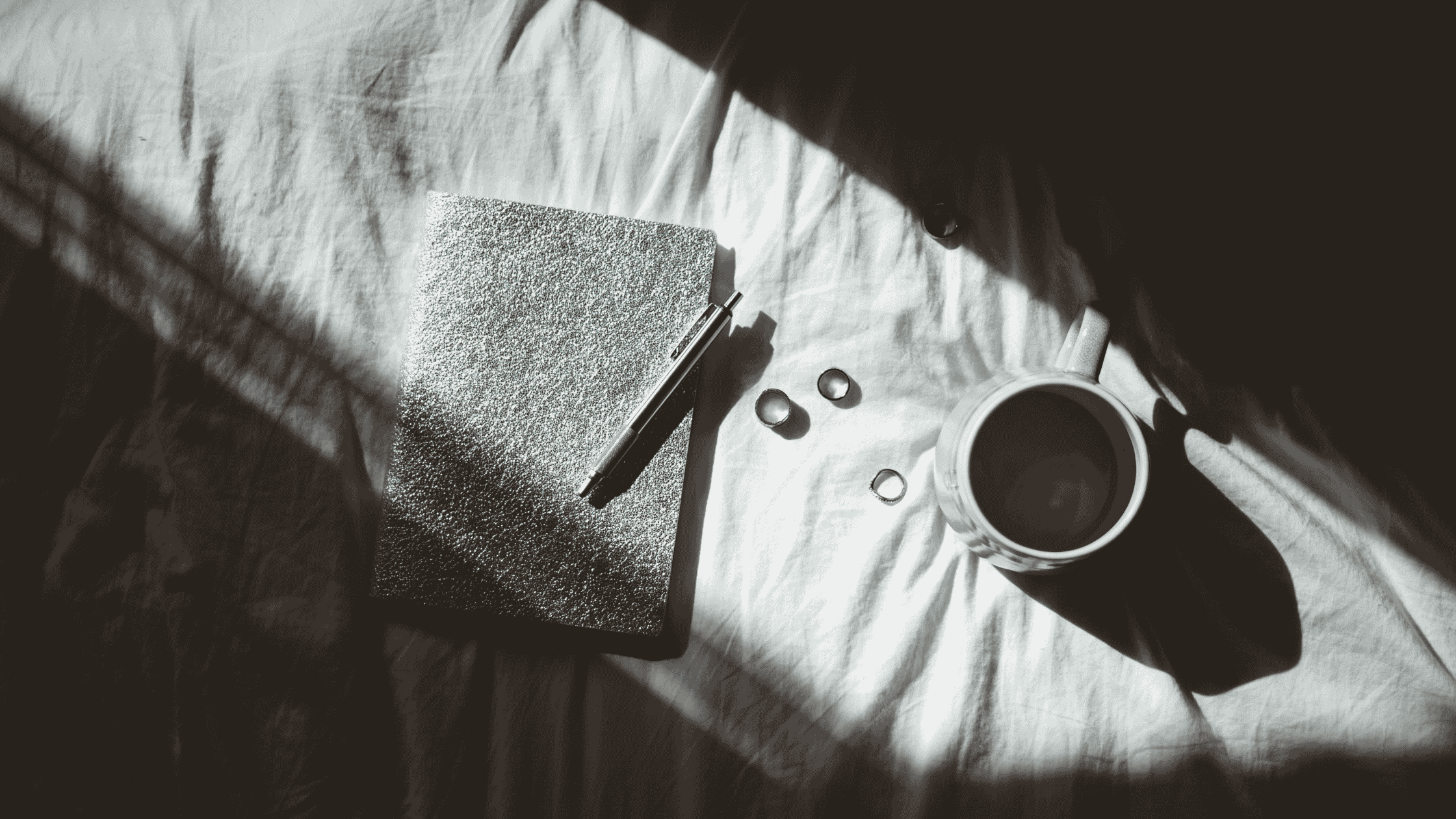 A black and white overhead photo of a textured journal and pen with dramatic light and shadows&mdash;evoking the introspective mood of shadow work journaling prompts
